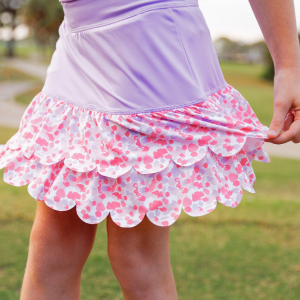 A young girl stands on a golf course modeling a pink polo shirt and a girls floral skort.