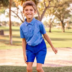 Two young boys stand on a golf course modeling blue striped polo shirts and chino shorts.