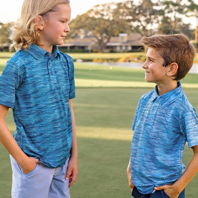 Two boys stand on a golf course modeling blue striped polos and chino shorts