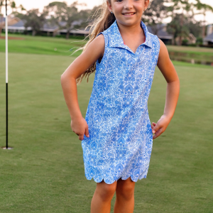 A young girls skipping on a golf course modeling a pink and blue floral tennis dress