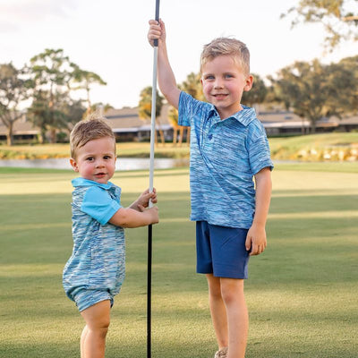 Two Toddler Boys stand on a golf course modeling light blue polo shirts and blue shorts