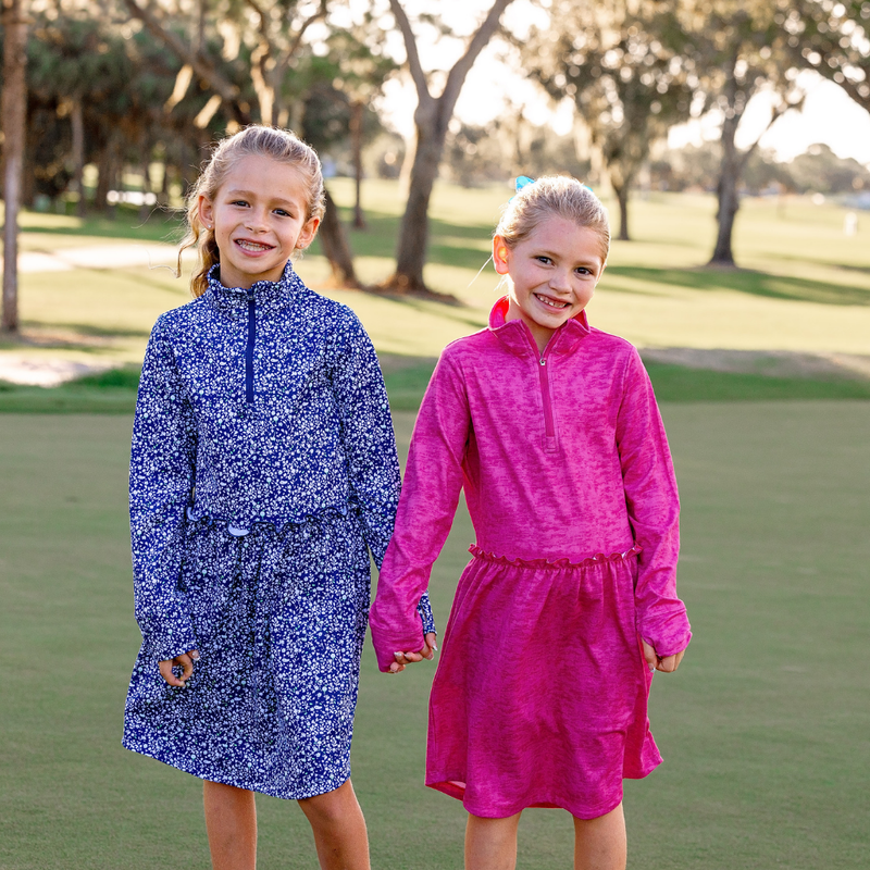 Two young girls wearing colorful Turtles and Tees golf dresses standing on a golf course.