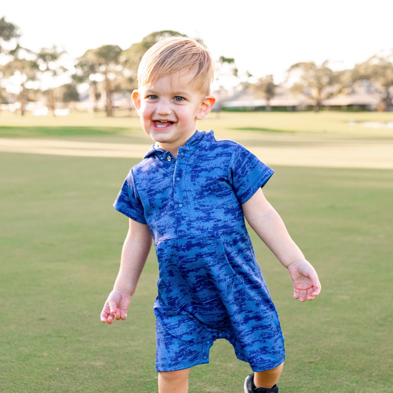 Child wearing a Turtles and Tees blue romper on a grassy field