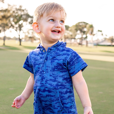 Child wearing a Turtles and Tees blue patterned outfit standing outdoors on a grassy area.