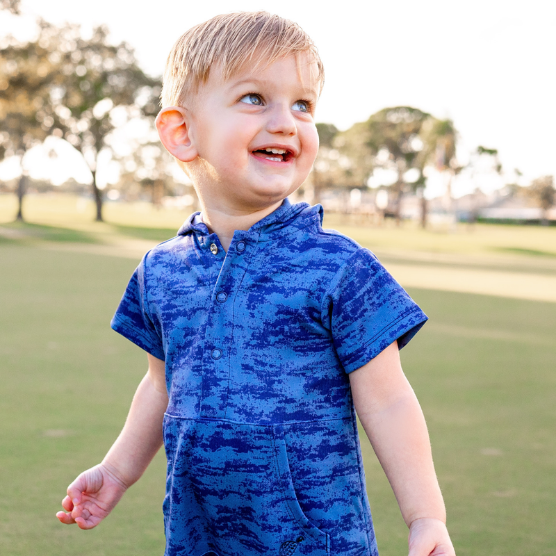 Child wearing a Turtles and Tees blue patterned outfit standing outdoors on a grassy area.