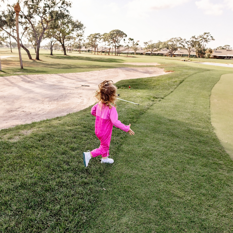 Toddler girl in a Turtles and Tees pink romper running outside on a golf course.