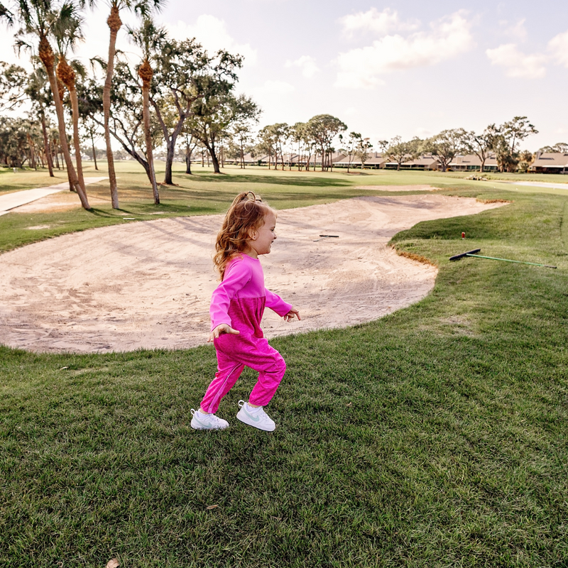 Toddler girl in a Turtles and Tees pink romper running outside on a golf course.
