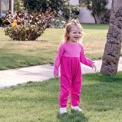 Toddler girl in a Turtles and Tees pink romper standing on grass with a tree and house in the background