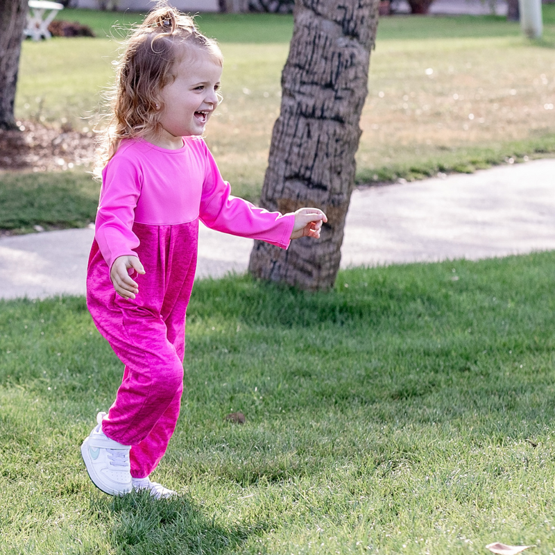Toddler girl in a Turtles and Tees pink romper standing in a golf course laughing.