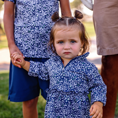 Toddler girl in a Turtles and Tees blue floral golf dress standing outdoors.