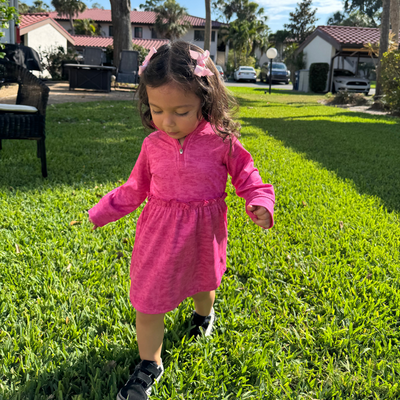 Child in a Turtles and Tees pink dress standing on grass with a residential background