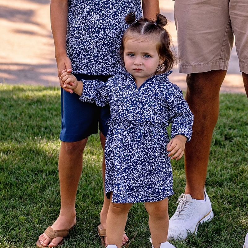 Toddler girl in a Turtles and Tees blue floral golf dress standing outdoors with adults