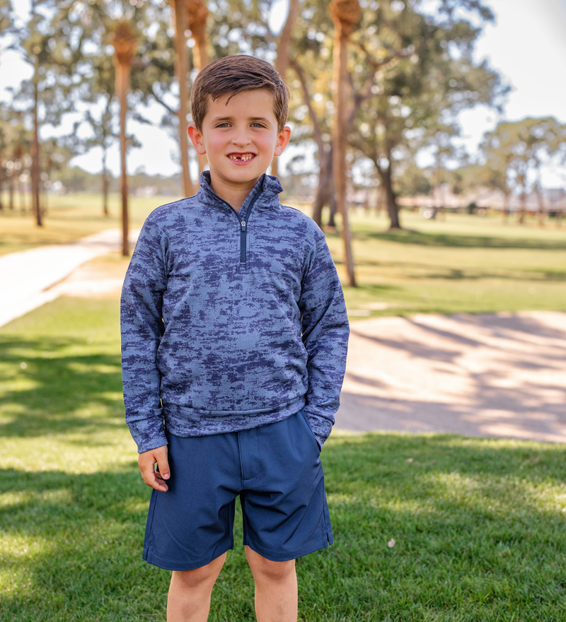 A young boy modeling a blue patterned golf pullover and navy blue golf shorts