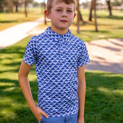 Young boy wearing a Turtles and Tees blue wave patterned shirt standing outdoors on grass.