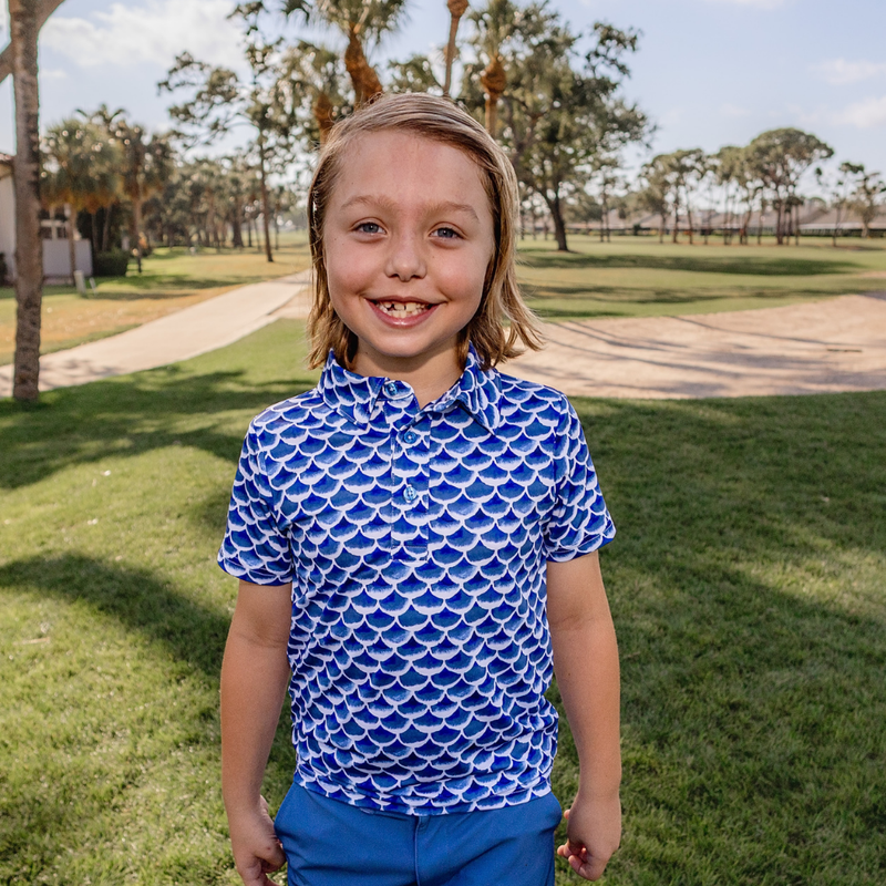 Child wearing a Turtles and Tees blue wave patterned golf shirt and blue pants standing in a park.