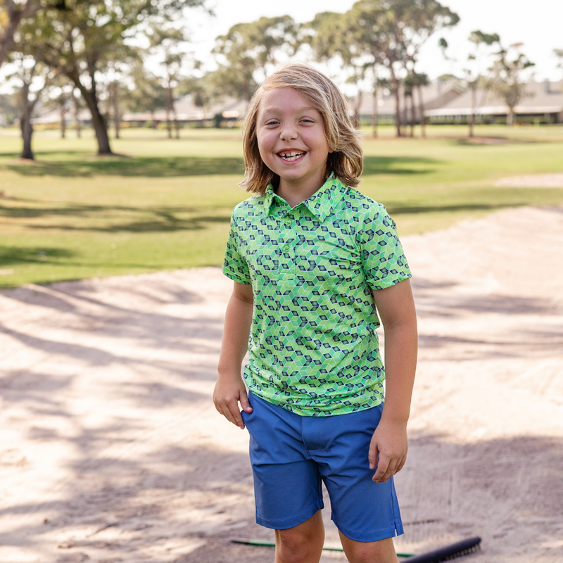 Child wearing a Turtles and Tees green patterned shirt and blue shorts standing on a golf course.