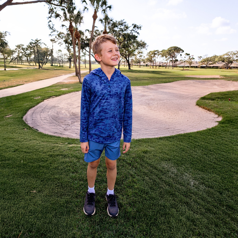 Child wearing a Turtles and Tees blue hoodie and shorts standing on grass with trees in the background