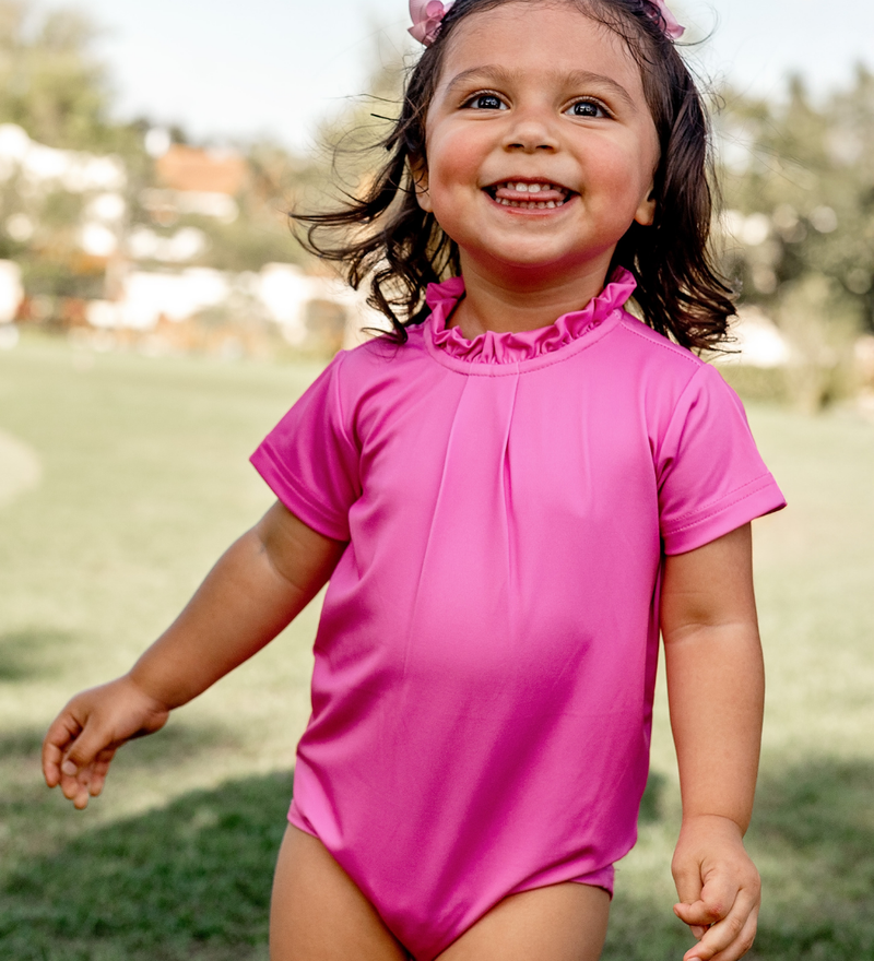 A toddler girl modeling a Turtles and Tees pink baby romper with ruffle collar