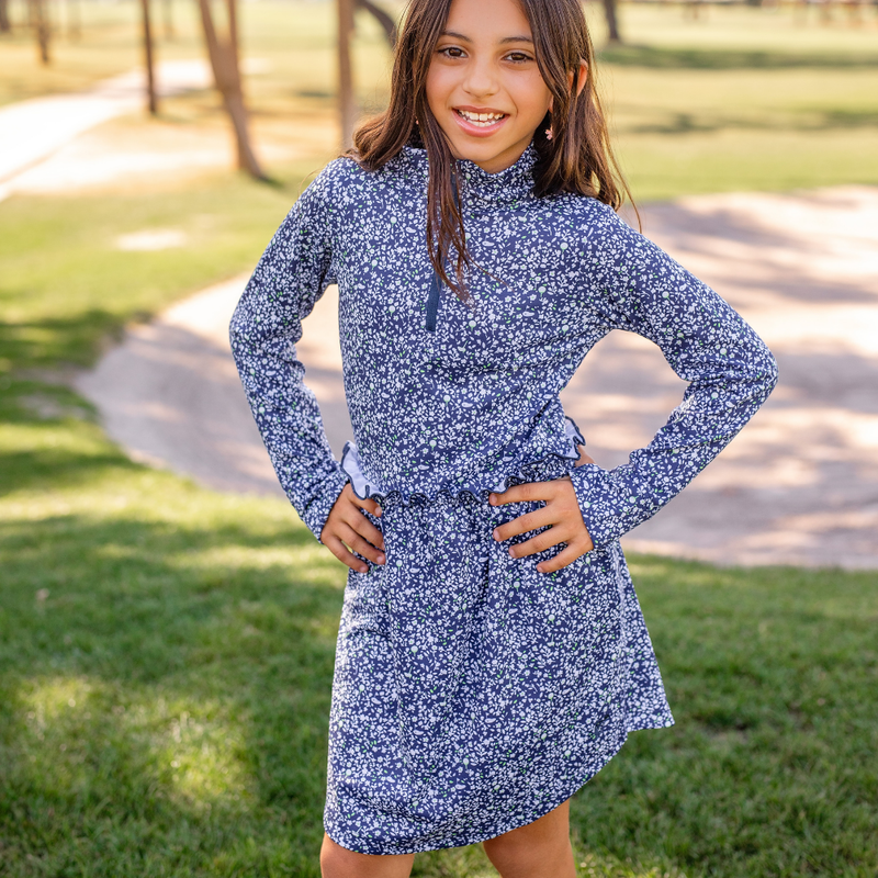 Young girl wearing a Turtles and Tees blue floral golf dress standing outdoors on grass.