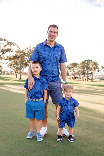 Man and two young boys in matching navy blue Turtles and Tees polo shirts standing on a golf course.