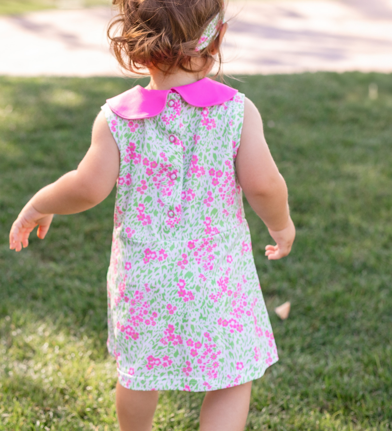 A toddler girl modeling a Turtles and Tees floral print pink and green infant and toddler romper and a floral bow headband