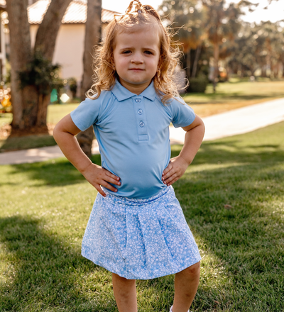 A toddler girl modeling a Turtles and Tees girls blue golf polo and blue floral girls skort
