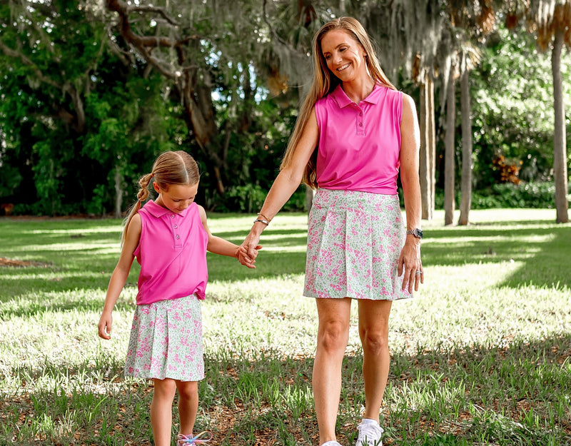 A young girl and a woman model matching mommy and me outfits of green and pink floral skorts and pink sleeveless polo shirts