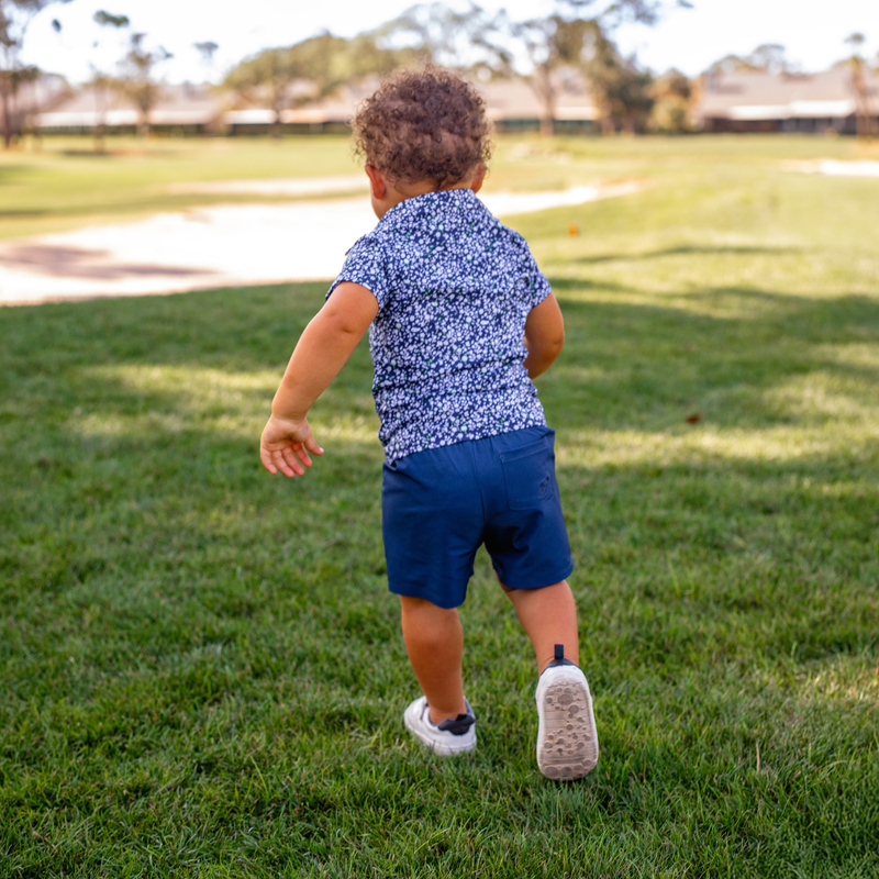 Toddler in a Turtles and Tees blue floral polo shirt and shorts running on grass
