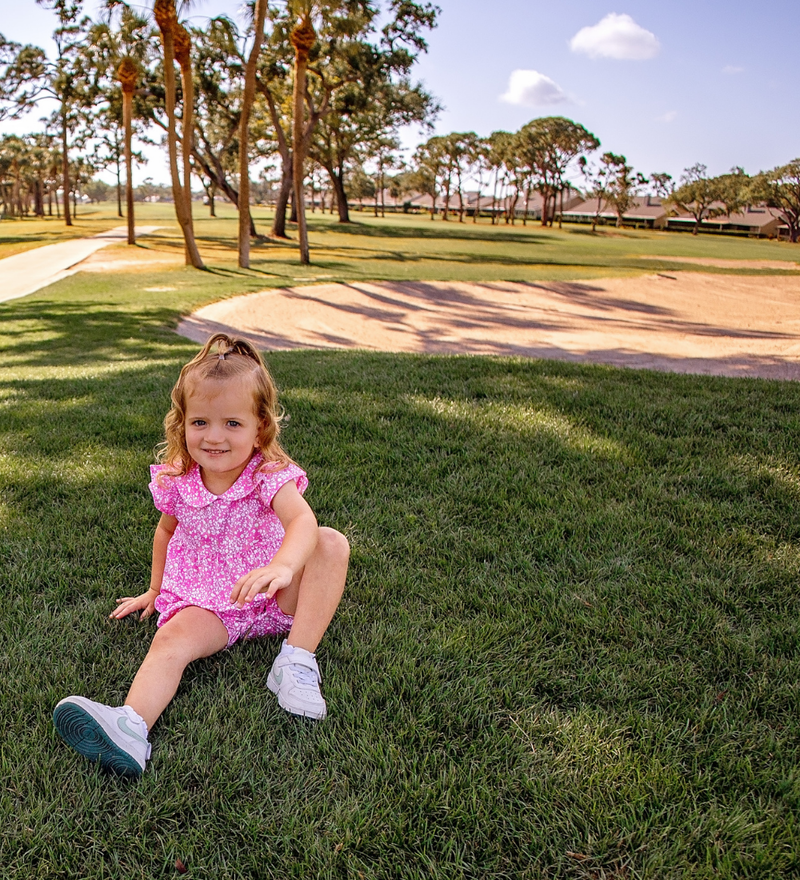 A toddler girl modeling a Turtles and Tees pink floral golf dress