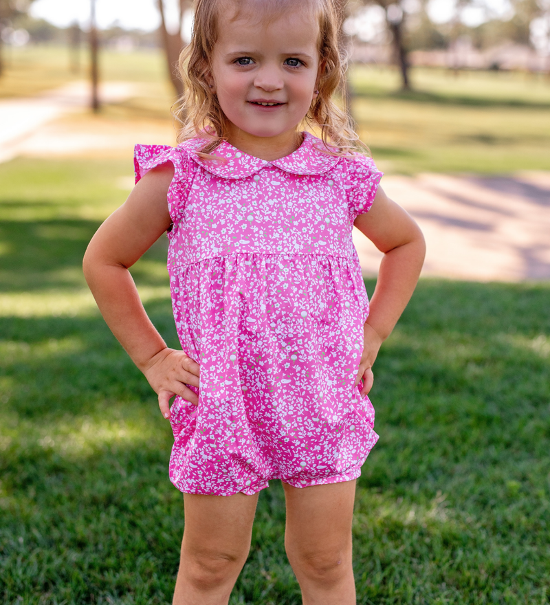 A toddler girl modeling a Turtles and Tees pink floral golf romper