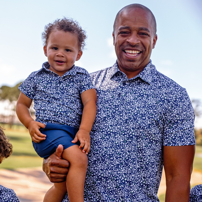 Man and toddler child wearing matching Turtles and Tees blue floral polo shirts outdoors