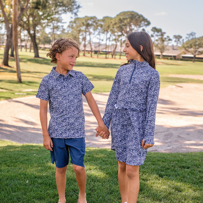 Two children in matching Turtles and Tees blue floral outfits standing on grass with trees in the background