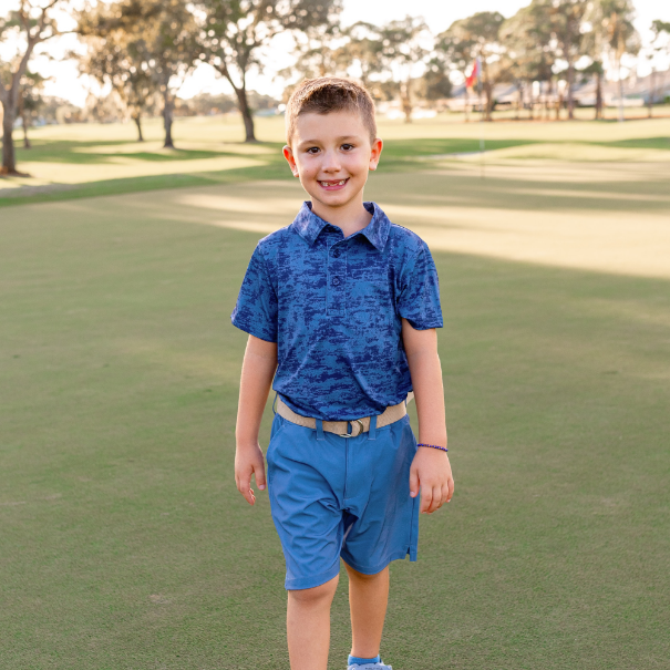 A young boy modeling a Turtles and Tees navy blue print polo and navy blue golf shorts