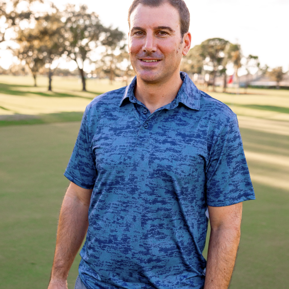 A man standing on a golf course modeling Turtles and Tees navy blue mens golf polo shirt
