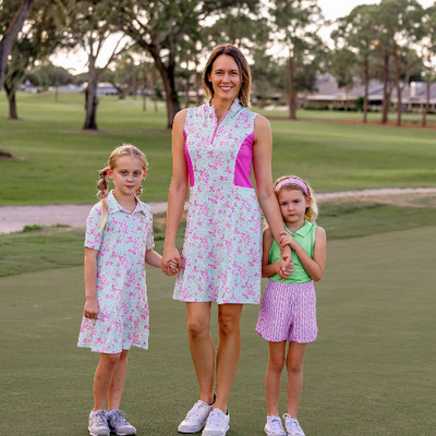 Two young girls and an adult woman stand on a golf course modeling matching mommy and me outfits in pink and green floral