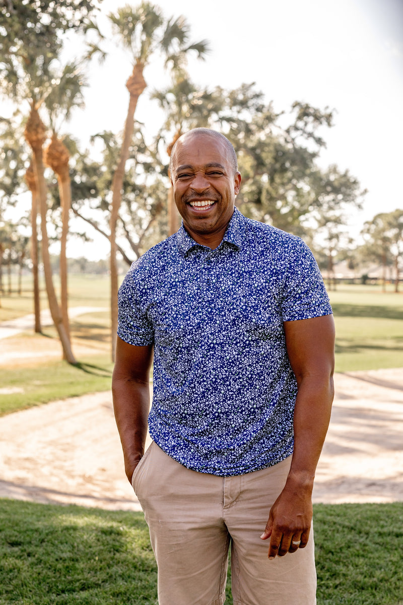 Man wearing a blue floral patterned Turtles and Tees shirt standing outdoors with trees in the background
