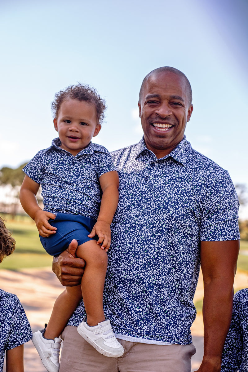 Man holding a child in Turtles and Tees matching blue floral outfits with a clear sky background